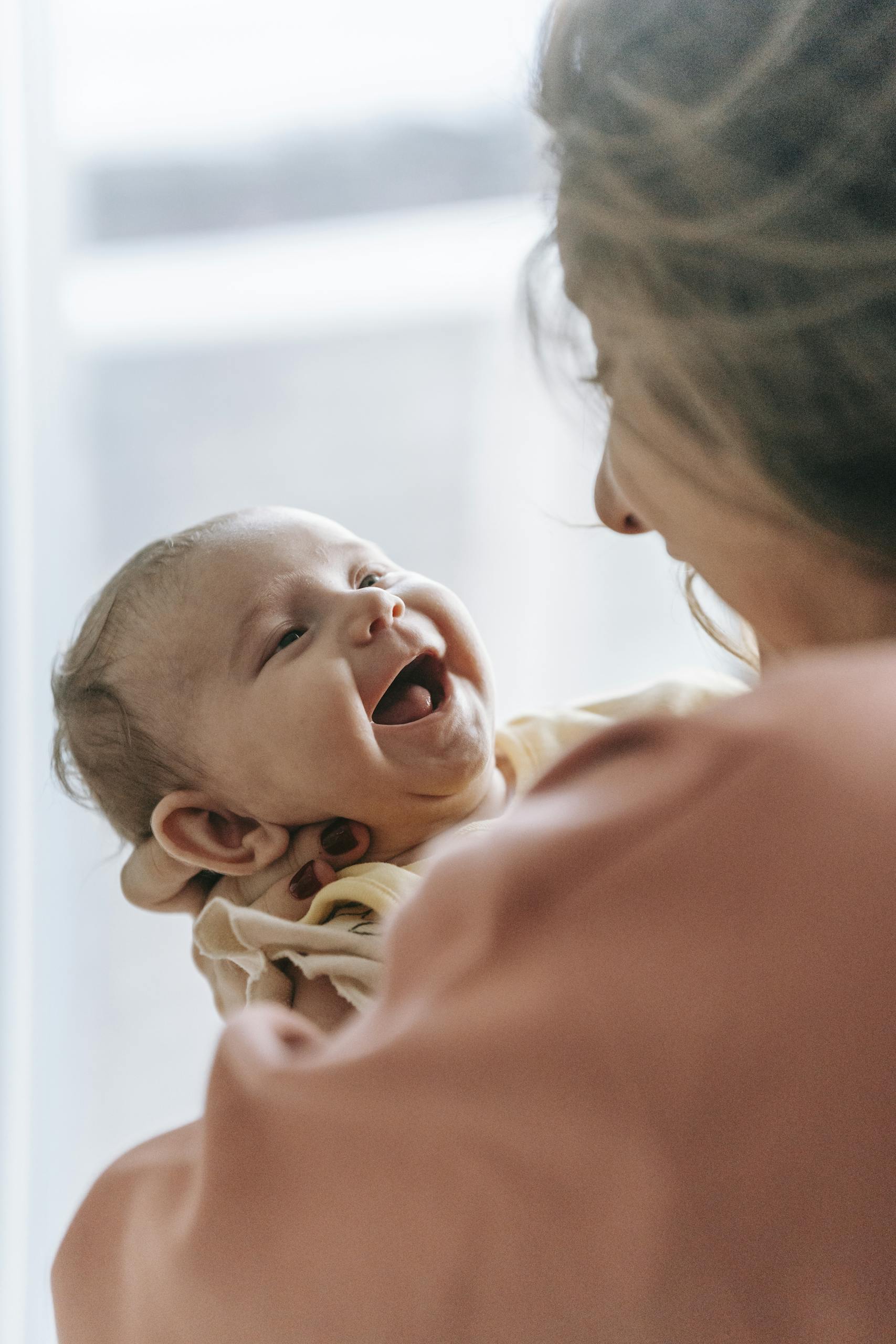A joyful moment of a mother holding a laughing baby in a cozy indoor setting.