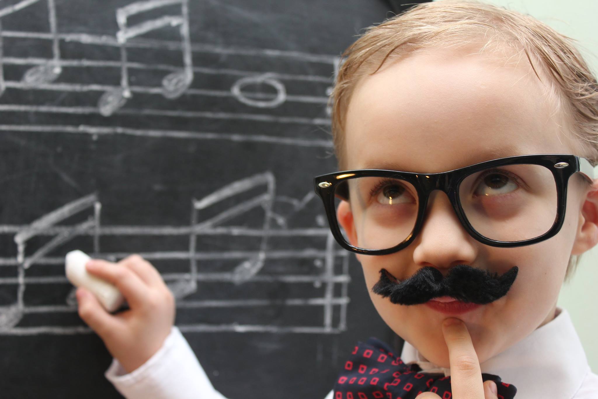 Little boy pretending to write music notes on a chalkboard.