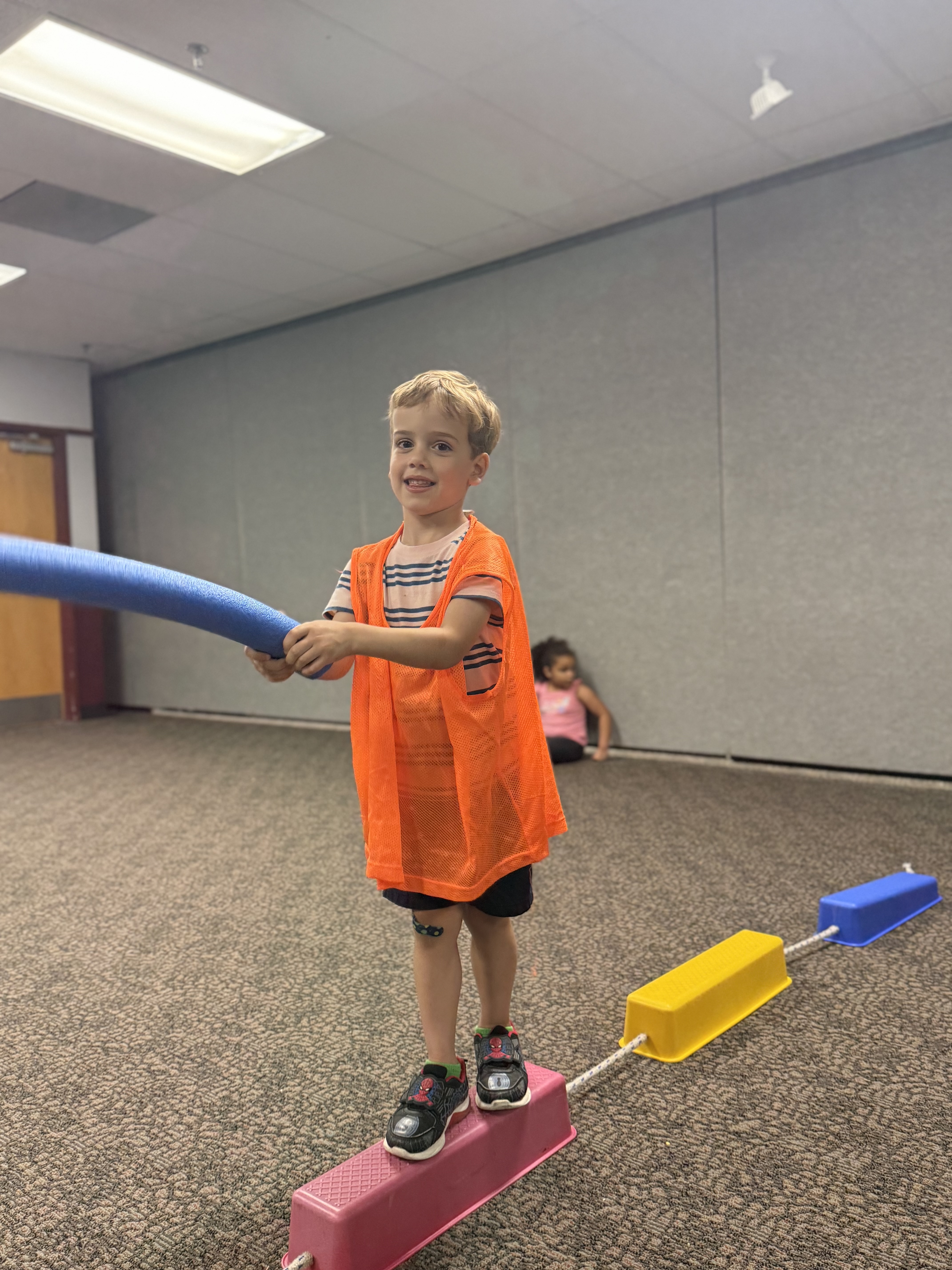 Child balancing on a beam while holding a pool noodle